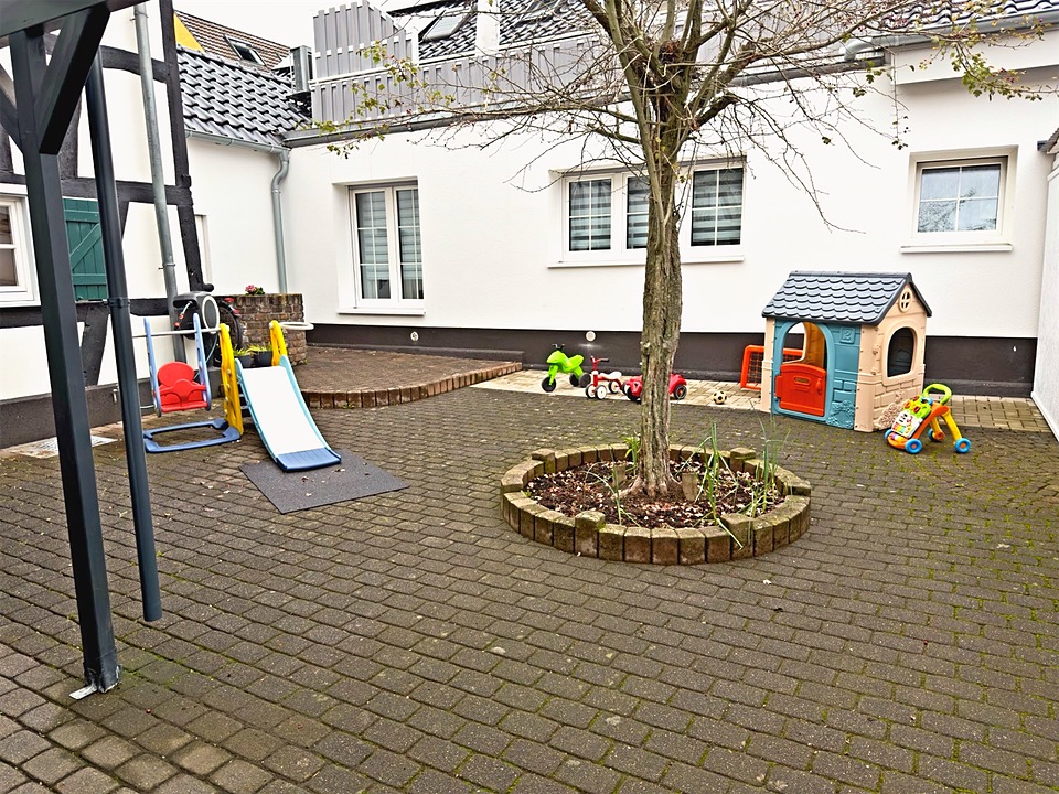Blick über den gepflasterten Hof mit Rutsche, Baum und Spielhaus